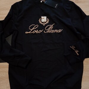 K&ouml;nnte beinhalten: Eine wei&szlig;e Keramik-Tasse mit schwarzem Henkel und dem Text "But first, coffee" in schwarzer, handschriftlicher Schrift. Die Tasse steht auf einer wei&szlig;en Oberfl&auml;che.