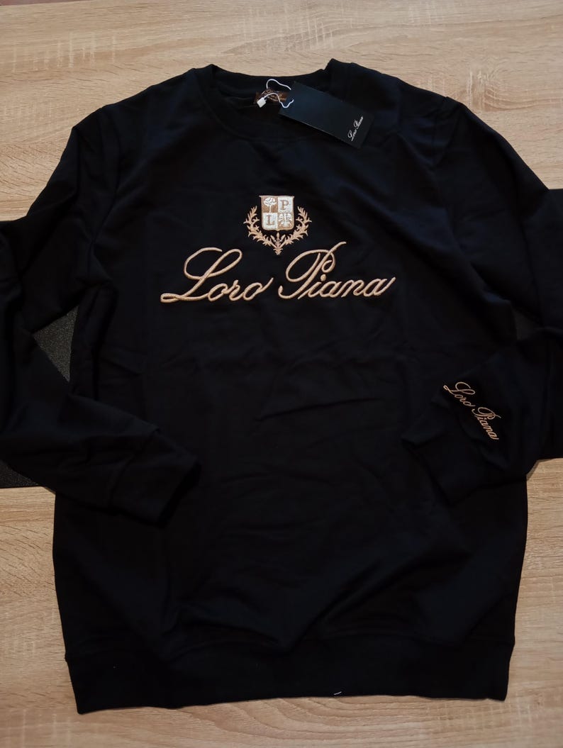 K&ouml;nnte beinhalten: Eine wei&szlig;e Keramik-Tasse mit schwarzem Henkel und dem Text "But first, coffee" in schwarzer, handschriftlicher Schrift. Die Tasse steht auf einer wei&szlig;en Oberfl&auml;che.