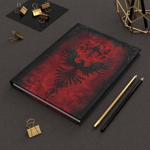 May include: A black and red journal with a black phoenix design and floral accents. The journal has a textured cover and a black spine.