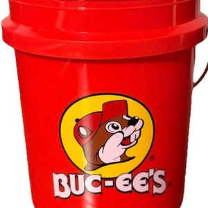 May include: A bright red bucket with a black handle. The bucket features a yellow circle with a cartoon beaver wearing a red hat and the text "BUC-EE'S" in white letters.
