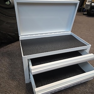 May include: White metal tool box with two drawers and a black foam lining. The top lid is open.