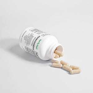 May include: A white bottle of Heal Thy Foods Ashwagandha capsules with black pepper, with several capsules spilled out. The bottle is tilted on its side, with the label visible. The capsules are light brown.