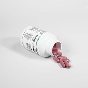 May include: A white bottle of beetroot capsules with the label "Heal Thy Foods" and "Beetroot" printed on it. The bottle is open and some of the red capsules have spilled out.