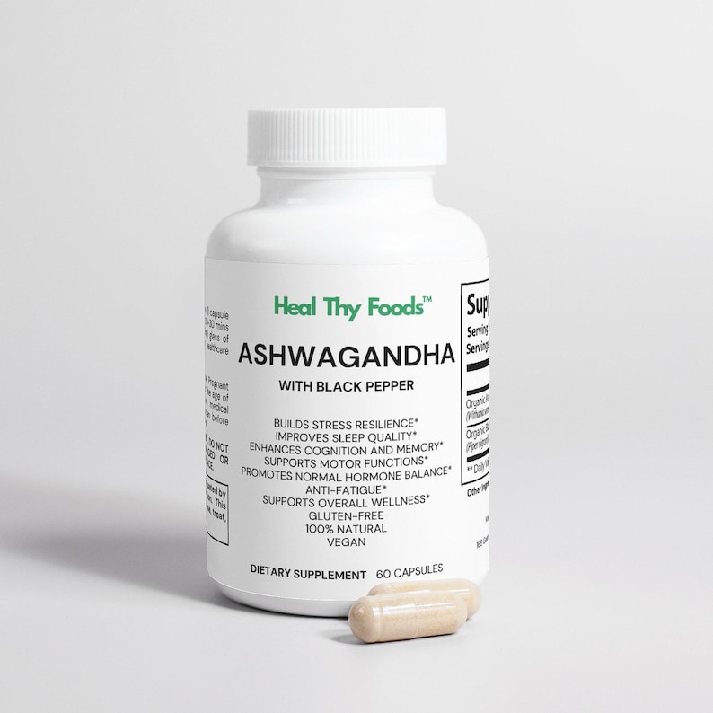 May include: A white bottle of "Heal Thy Foods" Ashwagandha capsules with black pepper. The bottle has a white cap and a label with text. Two capsules are next to the bottle. The capsules are beige.