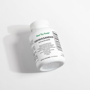 May include: A white bottle of Heal Thy Foods Ashwagandha with Black Pepper dietary supplement. The bottle has a white cap and is labeled with text including "Builds Stress Resilience" and "60 Capsules". The bottle is on a white surface.