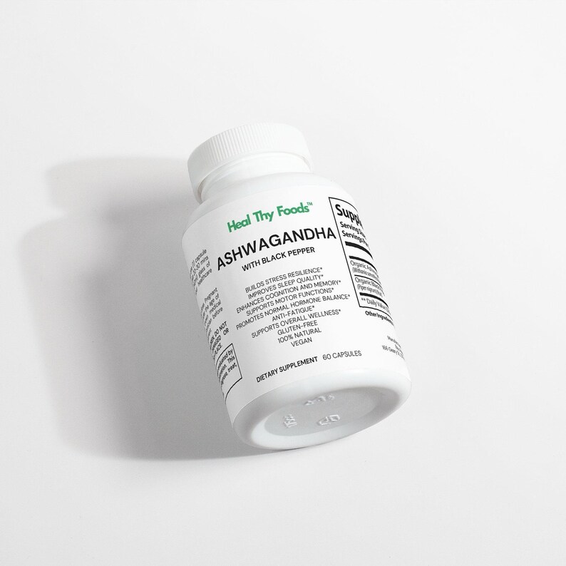 May include: A white bottle of Heal Thy Foods Ashwagandha with Black Pepper dietary supplement. The bottle has a white cap and is labeled with text including "Builds Stress Resilience" and "60 Capsules". The bottle is on a white surface.