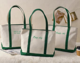 May include: Three canvas tote bags with white bodies and green trim. Each bag has green handles and embroidered text: "Shut Up No Way", "Easy day", and "Simply Me". A coffee cup sits nearby.