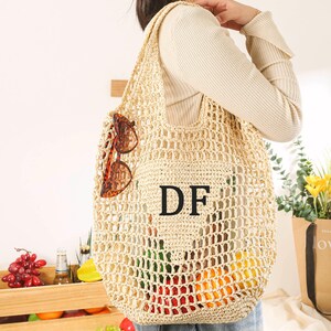 Puede incluir: Una bolsa de mano de crochet beige con las letras "DF" en negro en la parte delantera. La bolsa la lleva una persona que lleva un su&eacute;ter blanco. La bolsa est&aacute; llena de frutas y verduras.