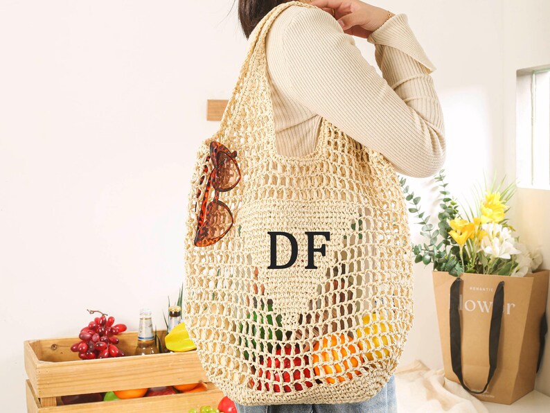 Puede incluir: Una bolsa de mano de crochet beige con las letras "DF" en negro en la parte delantera. La bolsa la lleva una persona que lleva un su&eacute;ter blanco. La bolsa est&aacute; llena de frutas y verduras.