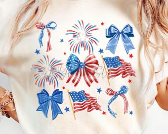 May include: Cream-colored t-shirt featuring a patriotic design. The design includes illustrations of blue bows, red and blue fireworks, American flags, and red and blue stars. The overall theme is a celebration of the United States.
