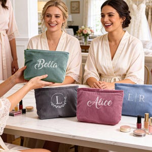 Peut inclure: Sacs &agrave; cosm&eacute;tiques en velours c&ocirc;tel&eacute; de diff&eacute;rentes couleurs, dont vert, gris, rose et bleu. Chaque sac est personnalis&eacute; avec un nom ou des initiales en &eacute;criture blanche. Les sacs sont pr&eacute;sent&eacute;s sur une table blanche avec des articles de maquillage.