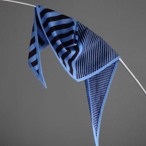 Pode incluir: Um cachecol triangular de malha com um padrão bicolor em azul claro e azul marinho escuro. Uma secção apresenta riscas horizontais largas, enquanto a outra metade transita para uma textura canelada fina e densa com riscas verticais finas.