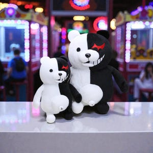 May include: Two plush bear toys, one large and one small, in a black and white colour scheme. The bears have a split design, with one side black and the other white. They have a red star on the black side and a smiling face.