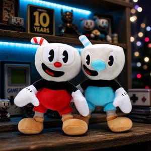 May include: Two plush toys featuring cartoon characters with cup-shaped heads. One character has a red straw, red shorts, and a black shirt. The other has a blue straw, blue shorts, and a black shirt. Both have white gloves, tan shoes, and wide smiles.