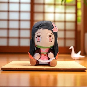 Op de afbeelding: Pluche pop van een anime-personage met zwart haar, roze ogen en een groene mondbeschermer. De pop draagt een roze kimono met een bruine jas en zit op een kleine mat. Een witte origami kraanvogel staat op de achtergrond.