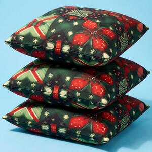 Puede incluir: Una pila de tres cojines cuadrados con un fondo verde oscuro y un patrón repetitivo de flores de pascua rojas, detalles en forma de estrella blancos y formas geométricas en tonos rojos, verdes y blancos sobre la superficie de la tela.