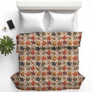 May include: A bed featuring a duvet cover with a repeating pattern of autumn maple leaves in shades of orange, red, brown, and cream. The bedding is paired with two solid white pillows, creating a seasonal look for a bedroom sleeping space.