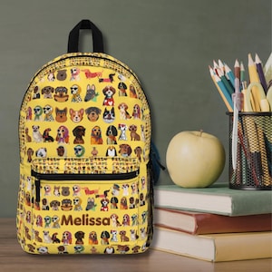 Puede incluir: Una mochila de color amarillo brillante con un patrón repetitivo de varias razas de perros, algunos con accesorios como bufandas y gafas de sol. El bolsillo delantero muestra el nombre Melissa en marrón oscuro. Asa y cremallera de color negro.