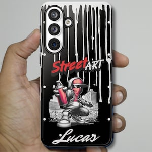 May include: Black phone case featuring a graffiti artist with a red spray can, the words "Street Art" in red and white, and the name "Lucas" in white script. The case has a black background with white drips.