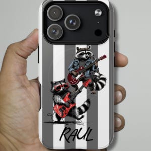 Puede incluir: Funda de teléfono con un diseño de dos mapaches tocando guitarras eléctricas rojas. Un mapache lleva gafas de sol. El fondo tiene rayas verticales grises y blancas. El nombre "RAUL" está escrito en escritura negra.