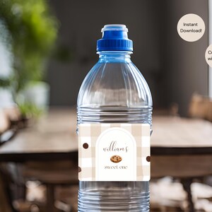 May include: A clear plastic water bottle with a blue cap. The label features a tan and white checkered pattern with the text "Williams Sweet One" and a cookie graphic. Two circular text bubbles are in the background.