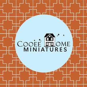 Può includere: Un cerchio blu chiaro con un contorno bianco e un'illustrazione in bianco e nero di una casa con il testo "COOEE HOME MINIATURES" in nero.