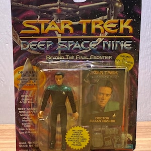 May include: A Star Trek Deep Space Nine Dr. Julian Bashir action figure in original packaging. The blister pack includes the figure, a collector card, and accessories. A ruler at the top shows the package is approximately 9 inches tall.