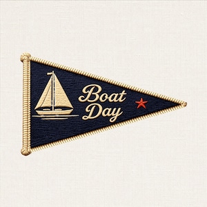May include: A triangular navy blue pennant featuring a beige embroidered sailboat graphic and the text "Boat Day" in beige script lettering. A small orange starfish is positioned to the right of the text. The edges are finished with beige rope.
