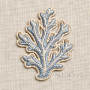 May include: An embroidered patch in the shape of a coral branch. The coral is light blue with beige accents and a beige border. The patch is on a beige fabric background. The text "PRESERVE EAST" is printed in a serif font.