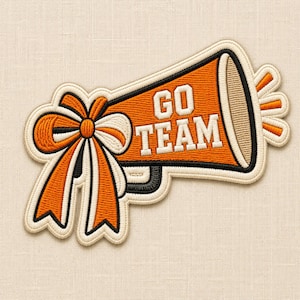 May include: An embroidered patch shaped like a megaphone in orange, white, and black thread. The megaphone features the text GO TEAM in white block letters. A large decorative bow in orange and white is attached to the side of the megaphone.