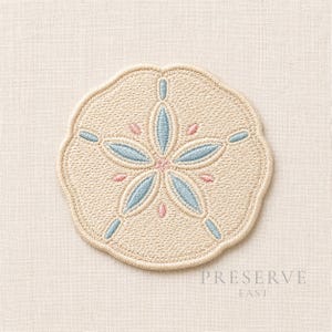 Puede incluir: Diseño bordado de dólar de arena en beige, azul claro y rosa. El dólar de arena tiene un borde festoneado y un patrón central en forma de estrella. El texto "PRESERVE EAST" está impreso en gris debajo.