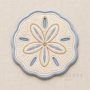 May include: A circular embroidered patch featuring a sand dollar design in cream, light blue, and gold thread. The patch has a scalloped edge outlined in light blue, with a central five-petal floral pattern and small oval accents in blue.