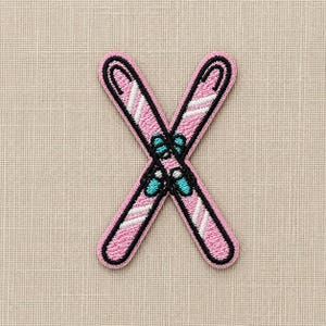 Puede incluir: Un parche bordado que muestra dos esquís cruzados de color rosa claro con rayas diagonales blancas. Los esquís están delineados con hilo negro e incluyen pequeñas fijaciones de esquí de color turquesa y blanco en el centro de la intersección.