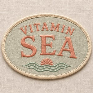 Könnte beinhalten: Ein ovaler, bestickter Aufnäher mit salbeigrünem Hintergrund und cremefarbenem Rand. Der Schriftzug VITAMIN SEA ist in korallenorangem Garn gestickt. Unter dem Text befinden sich eine kleine korallenorange Muschel und grüne Wellenlinien.