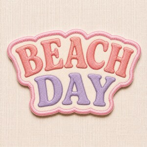 May include: An embroidered patch with a cream-colored background and a scalloped pink border. The text BEACH is stitched in coral pink thread, and the text DAY is stitched in lavender thread, both in a bold, rounded, sans-serif font style.