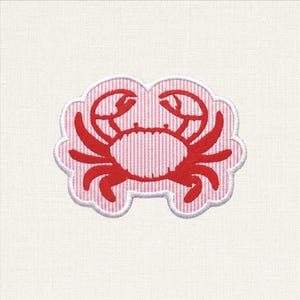 Puede incluir: Un parche de tela con la silueta de un cangrejo bordada en rojo, centrada sobre un fondo de rayas verticales finas en rosa claro y blanco. El parche tiene un borde festoneado con un acabado de costura blanca, creando una forma definida.