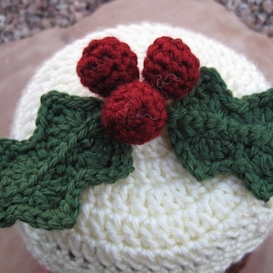 May include: White crocheted hat with red and green felt holly accents. The hat is shaped like a Christmas pudding.