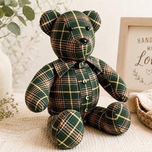 May include: A stuffed teddy bear crafted from dark green, yellow, and brown plaid fabric. The bear features a collar, three small buttons down the front, and black bead eyes and nose. It is constructed with visible seams and has a seated posture.