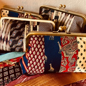 May include: Three colorful fabric clutches with gold metal frames. The clutches are made from repurposed neckties and feature a variety of patterns and colors, including blue, red, yellow, and brown.