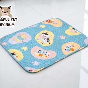 May include: A rectangular pet mat with a light blue quilted pattern. The mat features cartoon illustrations of a cow, a bear, and milk cartons. The mat has a white border and the word "Hello" is written on the mat.