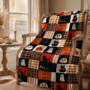 May include: A patchwork throw blanket featuring a repeating pattern of black cats, white ghosts, orange pumpkins, and plaid squares in black, orange, and white. Some squares include the word Spooky in white script text on an orange background.
