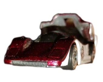 May include: A miniature toy race car with a maroon front and a silver and white body. The toy car has visible wheels and a detailed design, suggesting a vintage or collectible item.