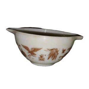 May include: Off-white vintage mixing bowl with a brown rim and decorative brown illustrations. The bowl features a pouring spout and is adorned with images of an eagle, corn, and other vintage-style graphics.