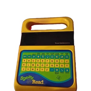May include: A yellow and black Speak & Read educational toy by Texas Instruments. The toy has a keyboard with letters and function buttons, and the text "Speak & Read" is displayed on the front.