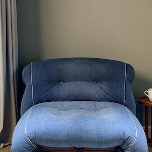May include: A denim armchair with a tufted back and seat. The chair features a two-tone design, with a darker blue denim on the back and a lighter blue denim on the seat. White piping outlines the edges.
