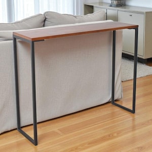 Puede incluir: Una mesa consola moderna con una tapa rectangular de madera oscura y una estructura de metal negro. La mesa está diseñada para colocarse detrás de un sofá, ofreciendo un diseño que ahorra espacio. La mesa mide aproximadamente 122 cm de largo.