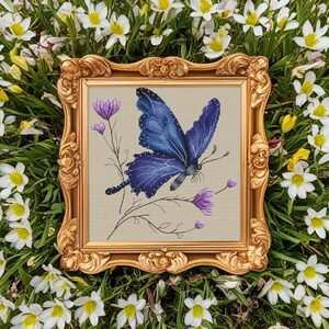 May include: A framed cross-stitch embroidery featuring a blue butterfly with purple accents, surrounded by delicate pink flowers on a beige background.