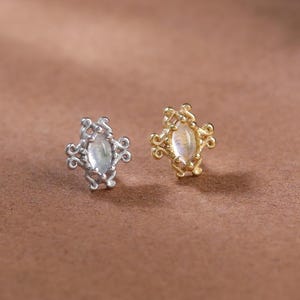 May include: Two stud earrings featuring a marquise-shaped iridescent stone set in a decorative metal frame with scrollwork details. One earring is silver-toned, and the other is gold-toned, both showcasing a central cabochon gemstone.