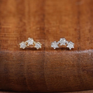May include: Two small stud earrings, each featuring a curved bar design set with three tiny, clear, round-cut stones. One earring is crafted from a warm yellow-toned metal, while the other is made from a cool silver-toned metal, both polished.