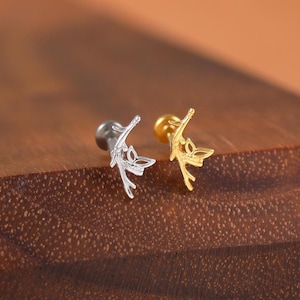 Può includere: Due piccoli orecchini decorativi. Uno è color argento con un perno nero, l'altro è color oro con un perno dorato. Entrambi gli orecchini presentano un delicato design traforato. Gli orecchini sono esposti su una superficie di legno scuro.